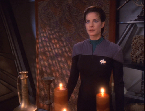 Jadzia stands in her uniform in her quarters behind two large candles