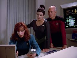Troi and Picard look over Crusher's shoulder