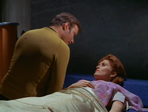 Kirk leans over Janice in bed