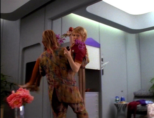 Neelix carries Kes out of her quarters, her clutching flowers
