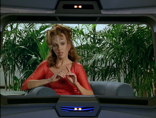 Alien woman with a vertical ridge on her forehead and palms in the background, seen on the Voyager viewscreen