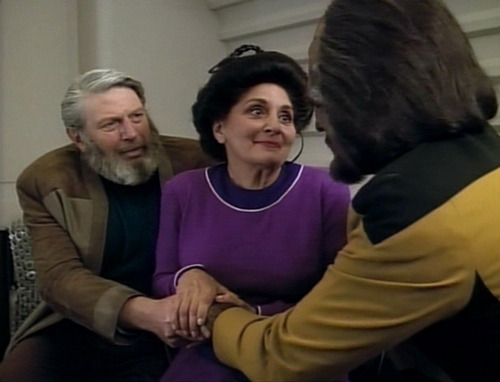 Worf's parents clasp his hands in a gesture of comfort and support, as they sit in his quarters