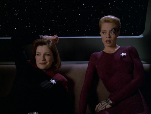 Janeway sits on a sofa next to Seven