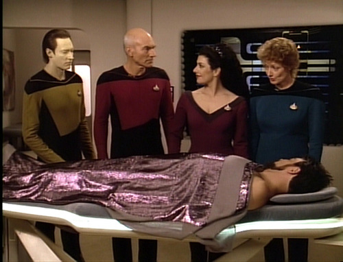 Data, Picard, Troi and Pulaski stand over a recovering Riker in Sickbay