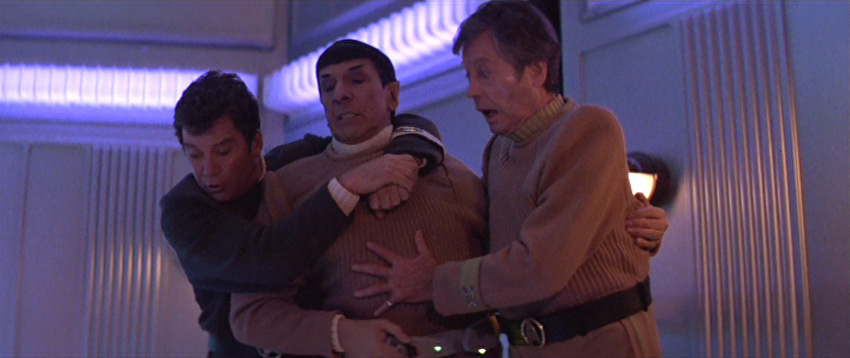 Kirk and McCoy hang on to Spock and look down