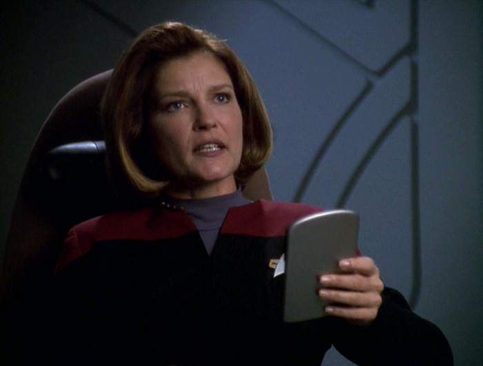 Janeway holds a padd and looks dismayed