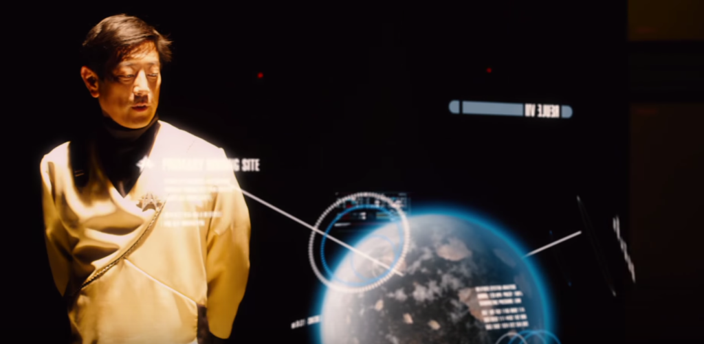 Grant Imihara as a Starfleet officer looking at a holographic projection of the planet