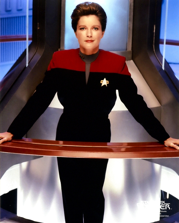 Janeway standing  in front of the warp core and leaning on the railing
