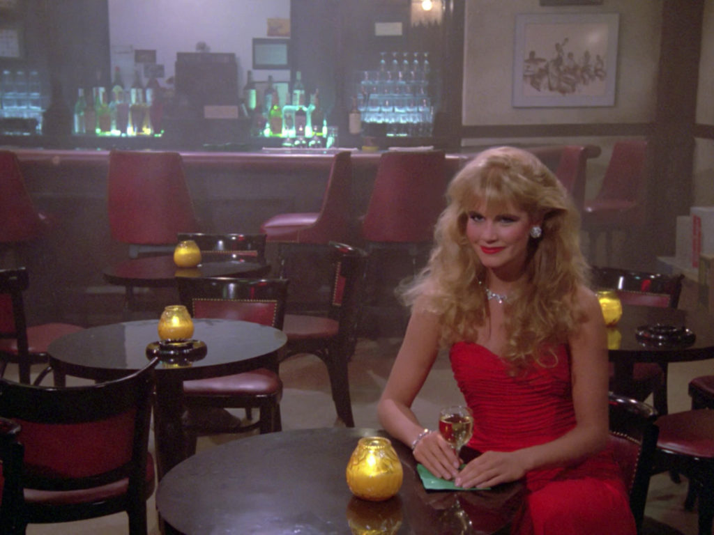 A blonde woman in a red dress sits in the holodeck jazz club