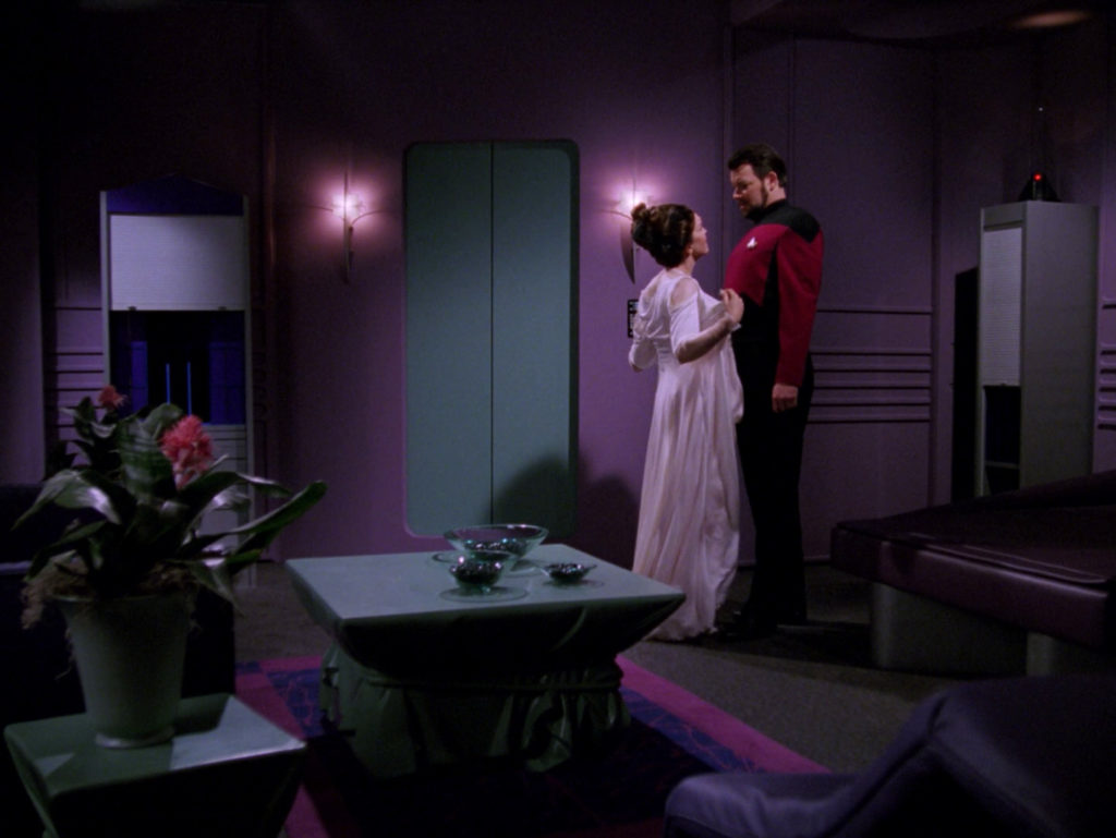 Manua stands close to Riker and starts to remove her robe