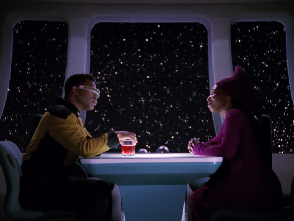Geordi and Guinan sit across a table in 10 forward