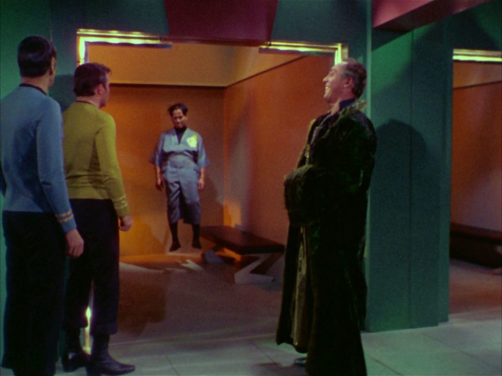 Garth, Kirk and Spock look at Governor Cory through the glass door of his holding cell
